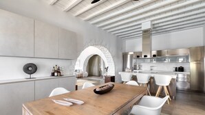 A modern kitchen with a central island, white chairs, and a wooden dining table. - Villa Santa Bliss Paros (Paros)