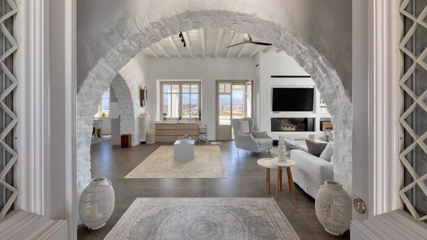 A spacious living area with a white archway, a sofa, a coffee table, and a TV. - Villa Santa Bliss Paros (Paros)