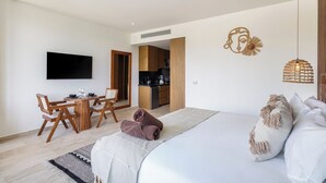 Et moderne hotelværelse med seng, skrivebord med stole, tekøkken og et fjernsyn monteret på væggen.