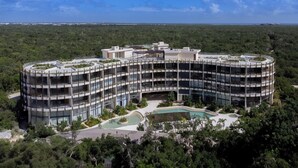 Et moderne hotel i flere etager med en buet arkitektur, der inkluderer en central gårdhave med swimmingpool og frodig beplantning.