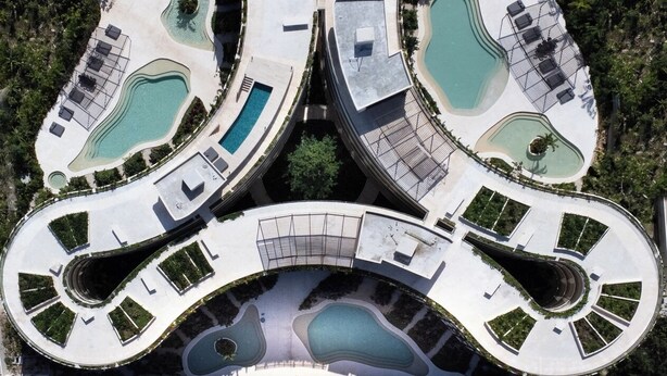 Et symmetrisk, moderne resort med flere swimmingpools, liggestole og en central sti.