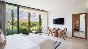 Et moderne soveværelse med en stor seng, et spiseområde med træmøbler, et fjernsyn monteret på væggen og en balkon med udsigt over grønne områder og bygninger.