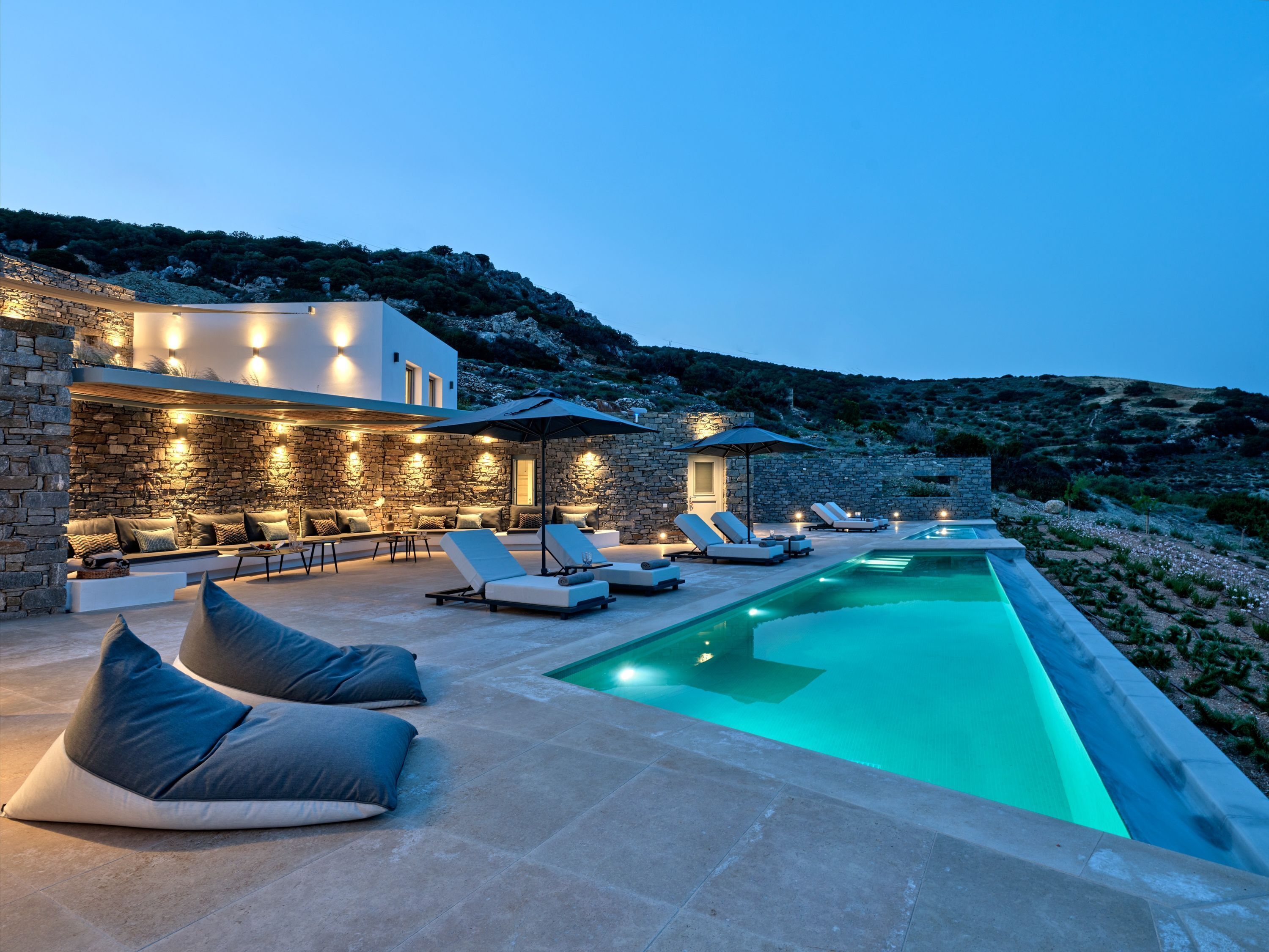 A modern outdoor pool area with stone walls, lounge chairs, and a stone bench.