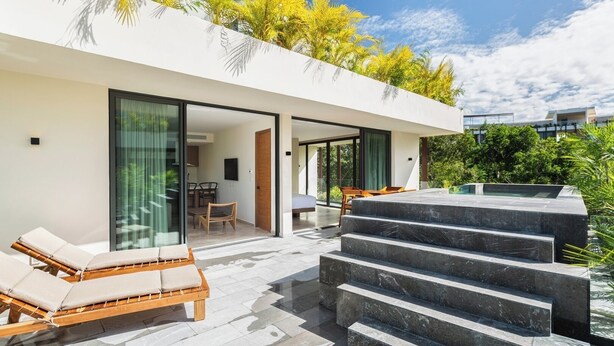 A modern villa with a glass-enclosed patio, a wooden lounge chair, and a set of stone steps leading to a pool area. - Fast Wi-Fi, private pool, A/C and jungle view! (Tulum)