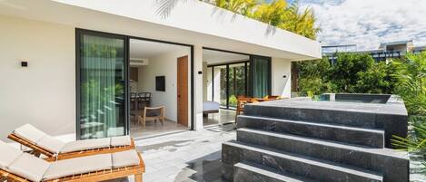 Une villa moderne dotée d’un patio entièrement vitré, d’un fauteuil de salon en bois et d’un escalier en pierre menant à une zone de piscine.
