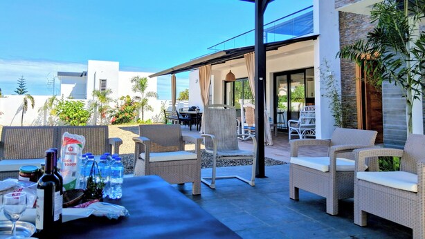 An outdoor patio area with wicker furniture, a table set with bottles and glasses, and a view of the surrounding buildings and sky.