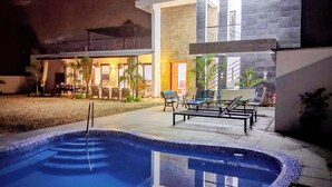 A swimming pool with a tiled edge, surrounded by a patio area with outdoor furniture.
