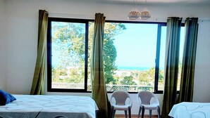 A hotel room with two beds, a view of the sea, and a balcony with chairs.