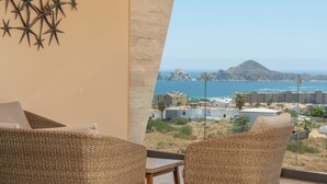 Ein Balkon mit Korbstühlen, Blick auf das Meer und Gebäude in der Ferne.