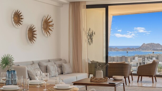 Ein modernes Wohnzimmer mit Sofa, Esstisch und Blick auf das Meer sowie die Stadtlandschaft durch große Fenster.