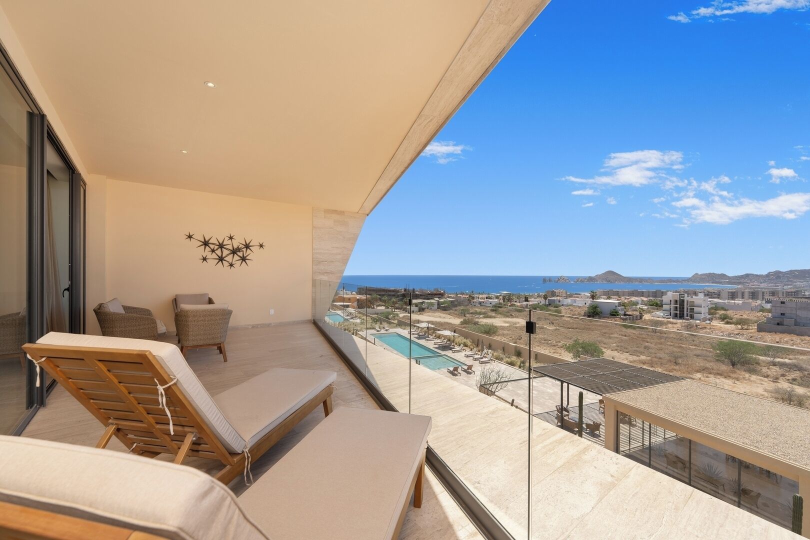 A balcony with lounge chairs, a pool, and a view of the sea and buildings.