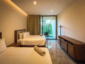 A modern hotel room with two beds, a wooden dresser, and a large sliding glass door leading to a balcony with a view of greenery. - Perfect for family trips! 2 bedroom 3 beds AP (Tulum)