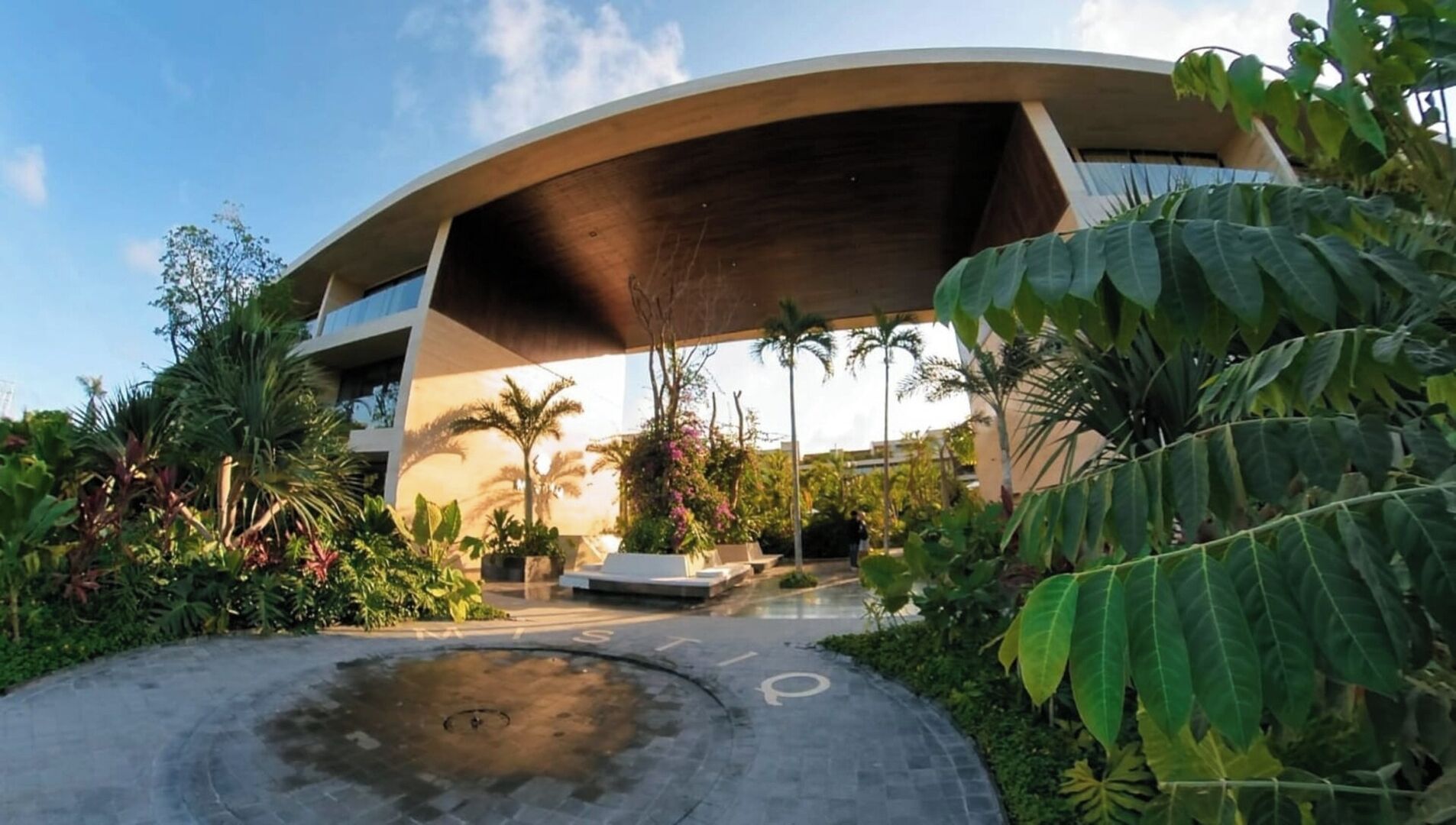 Un bâtiment moderne doté d’un toit incurvé et d’un espace jardin agrémenté de diverses plantes, ainsi que d’un coin salon.