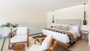 A modern bedroom with a large bed, two wooden chairs, a small table, and a potted plant. - Loft w/ Private Patio, 7 Pools, Gym and WiFi and AC (Tulum)