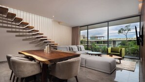 A modern living room with a wooden dining table, grey sofas, and a staircase with wooden steps. - Bright 3BR PH, Private Pool, AC and Pool View (Tulum)