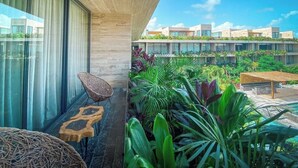 A balcony with a view of a modern building, surrounded by lush greenery and outdoor furniture. - Bright 3BR PH, Private Pool, AC and Pool View (Tulum)
