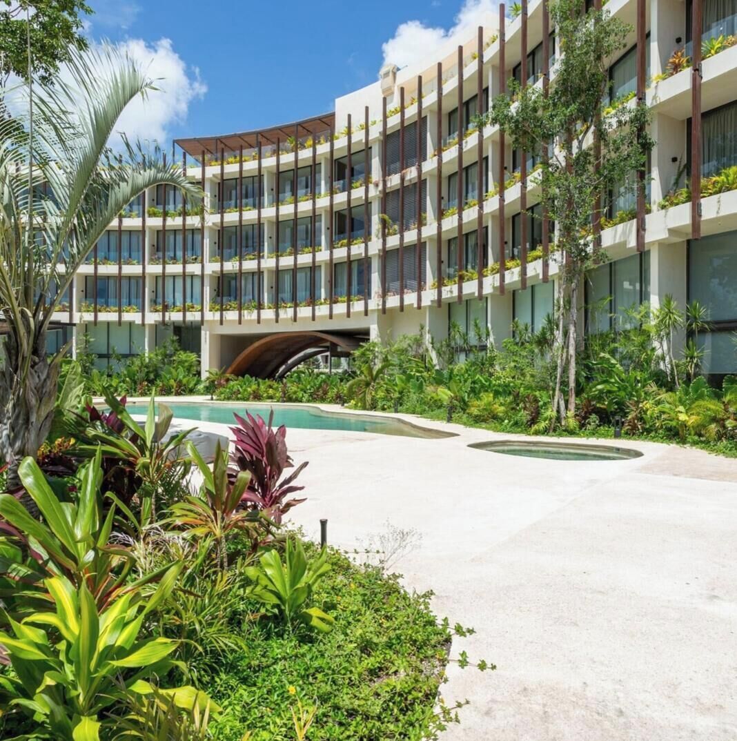 Et moderne hotel med flere balkoner, swimmingpool og frodig beplantning.