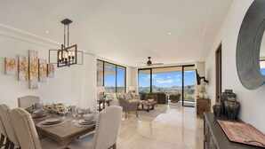 A spacious dining area with a high table set for six, flanked by two large windows offering a view of the landscape. - Ocean view, fast Wi-Fi, shared pool and BBQ (Cabo San Lucas)