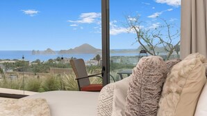 A room with a large window offering a view of the sea and distant islands. - Ocean view, fast Wi-Fi, shared pool and BBQ (Cabo San Lucas)