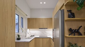 Eine moderne Küche mit Holzschränken, einem Edelstahlkühlschrank, Marmorarbeitsplatten und einer kleinen Pflanze im Regal.