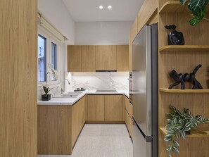 Uma cozinha moderna com armários de madeira, geladeira de aço inoxidável, bancadas de mármore e uma pequena planta na prateleira.