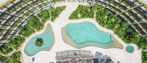 A rooftop pool area with two pools, surrounded by greenery and a covered seating area.