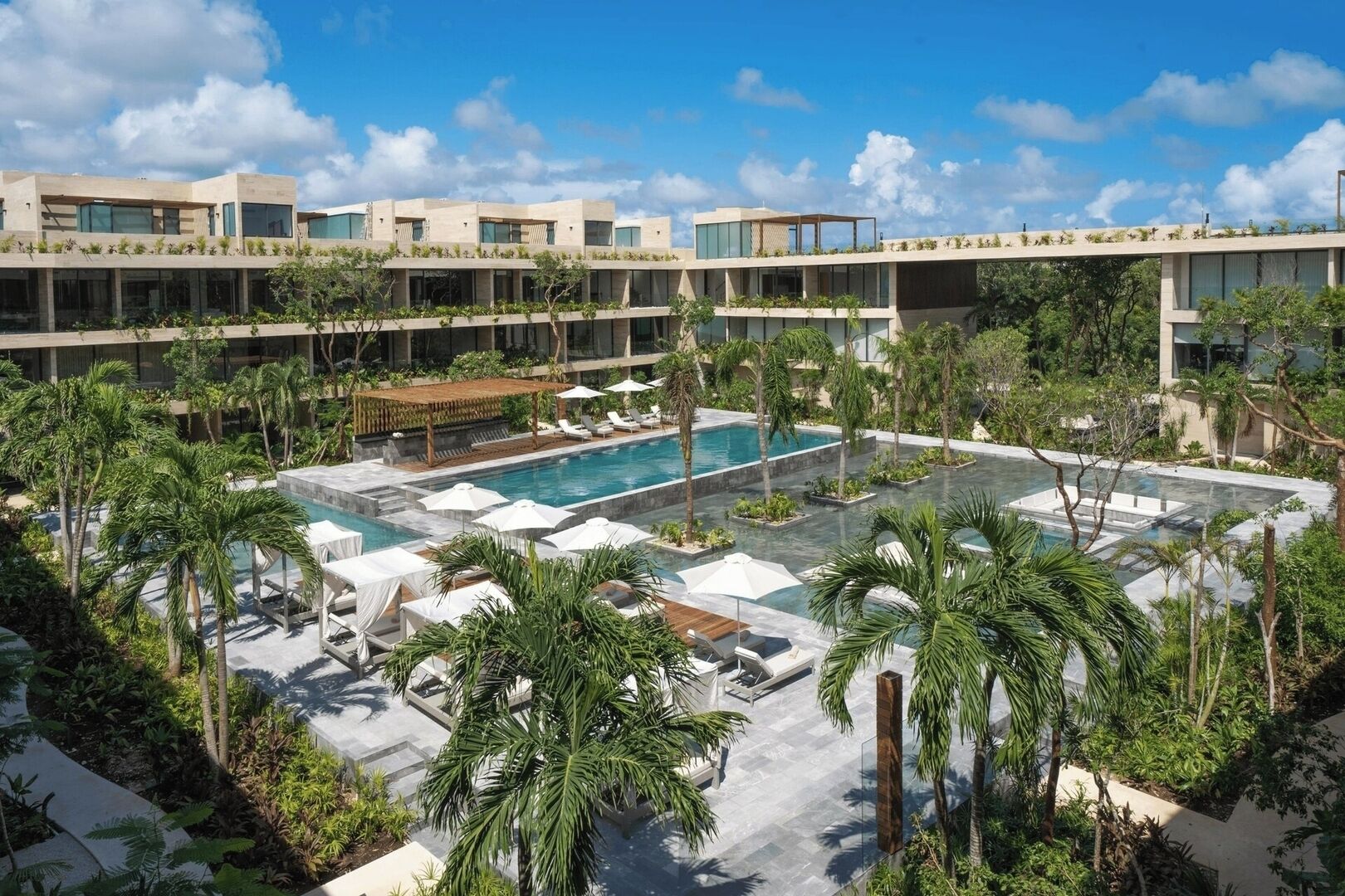 Un hôtel moderne doté d’une piscine centrale, entourée de palmiers et de chaises longues.