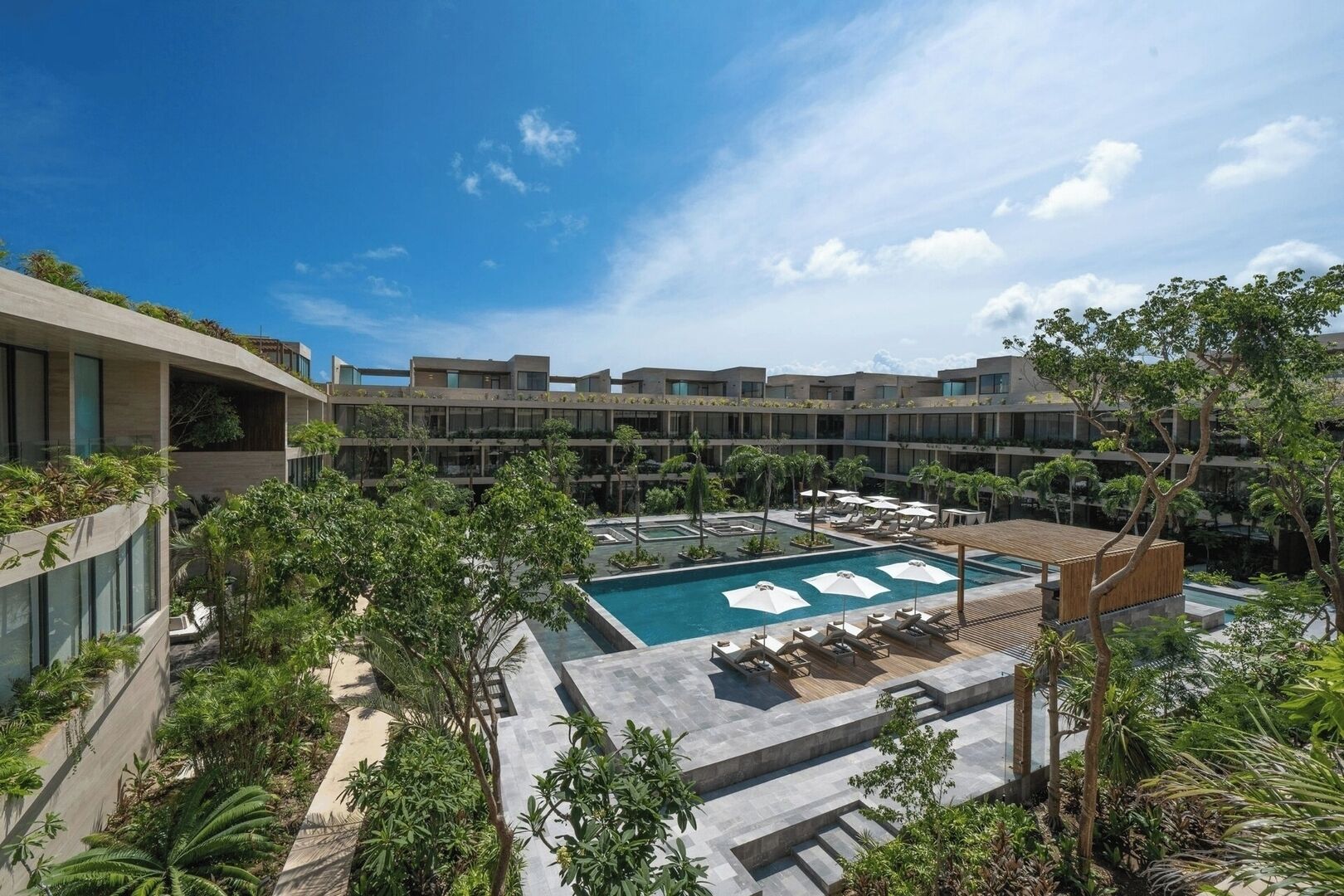A modern hotel with a central swimming pool, multiple balconies, and lush greenery.