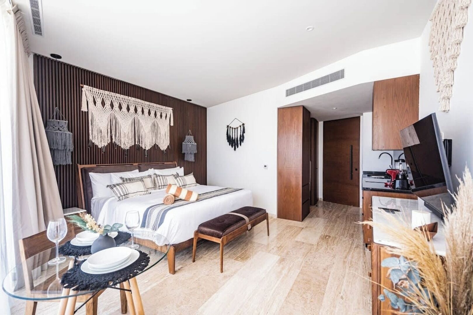 A modern bedroom with a bed, bedside tables, a desk, and a kitchenette.