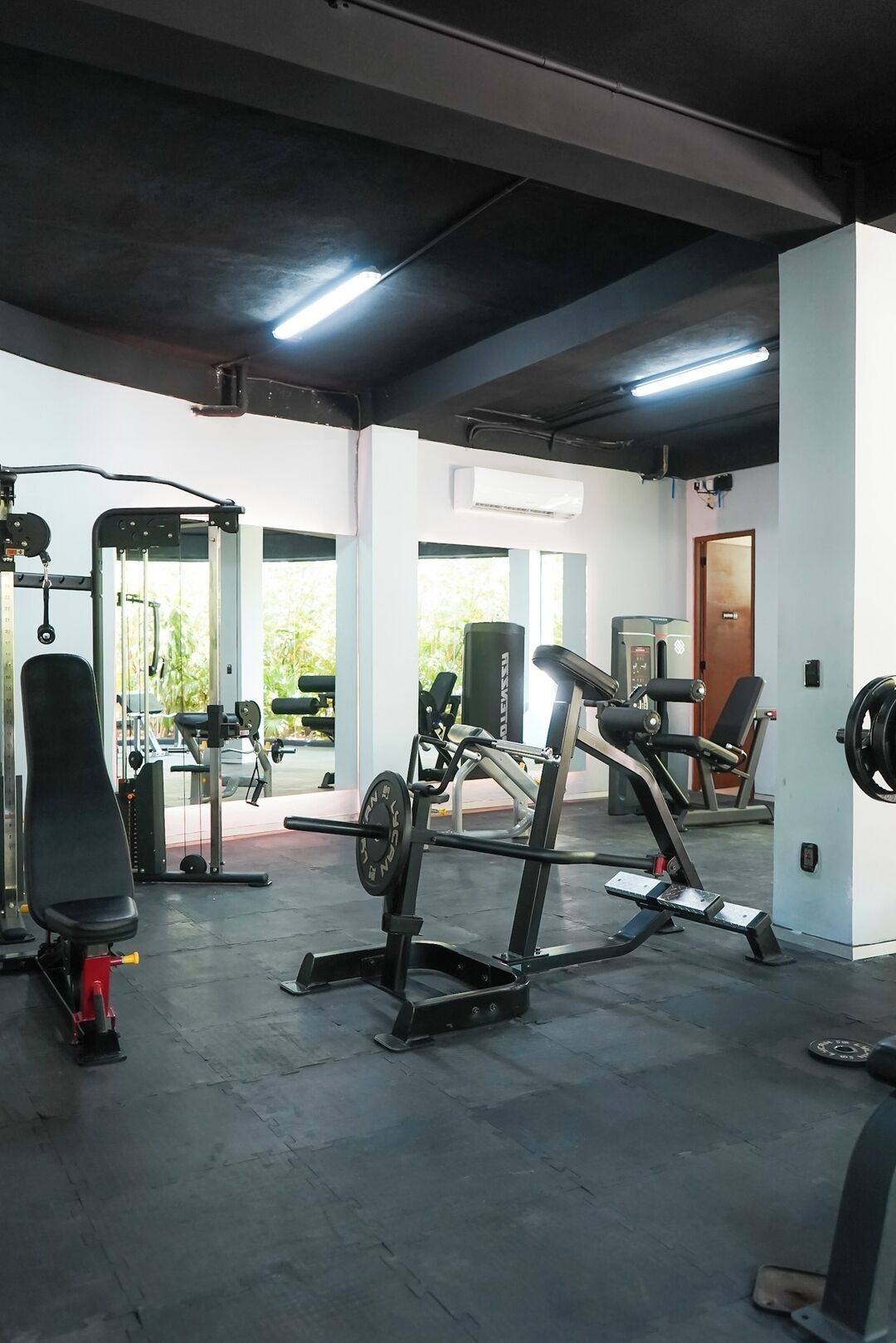 Ein Fitnessraum mit unterschiedlichen Trainingsgeräten, darunter eine Langhantelbank, ein Squat-Gestell und eine Gewichtbank.