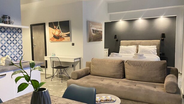 Ett modernt hotellrum med en säng, en soffa, ett skrivbord och en stol. Det finns konstverk på väggarna och en växt.