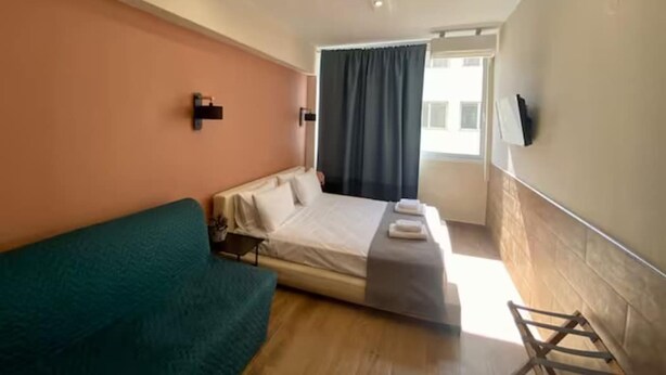 Une chambre à coucher avec un lit, un canapé de couleur turquoise, une petite table et un téléviseur fixé au mur.