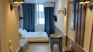 A compact hotel room with a bed, a small table, a chair, a mirror, and a wardrobe. - Monastiraki 306 @SuperHost Hub (Athina)