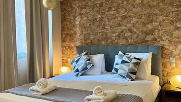 A hotel room with a stone wall, a large bed with a blue headboard, two bedside lamps, and a window with curtains.