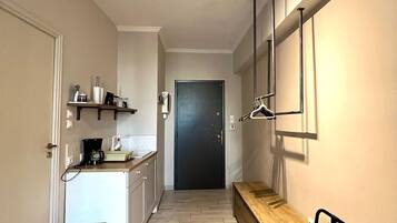 A narrow hallway with a kitchenette on the left, a bench on the right, and a door at the end.