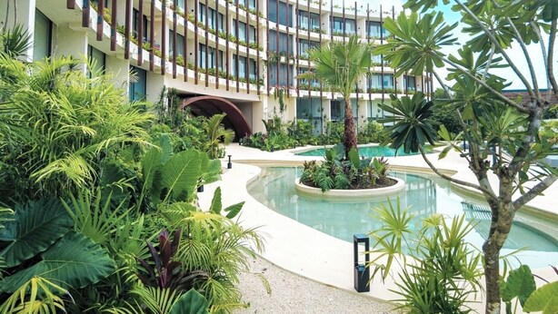 Un hotel con un edificio a forma di curva, una piscina e una rigogliosa vegetazione tropicale.