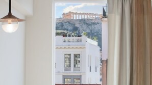 Uitzicht vanuit een raam met gordijn, op een gebouw met pannendak en een balkon.