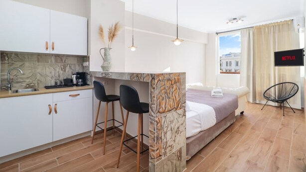Een kleine hotelkamer met kitchenette, een bed, een televisie en uitzicht over de stad.