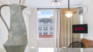Een moderne kamer met een marmeren tafel, een bijzondere vaas, uitzicht op gebouwen, een Netflix-bord en een hanglamp.
