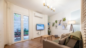 Una sala de estar moderna con televisor, sofá, una mesita y un balcón con vista al mar.