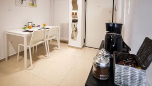 Una stanza piccola e pulita con un tavolo e sedie bianche, una macchina per caffè e un cesto di snack.
