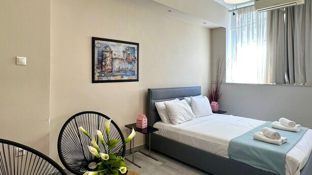Un dormitorio moderno con cama, escritorio, sillas, una planta en maceta y un cuadro en la pared.