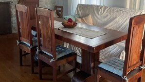 Ruokailutila, jossa on puinen pöytä ja tuolit, kiviseinä sekä ikkuna, jossa on verhot.