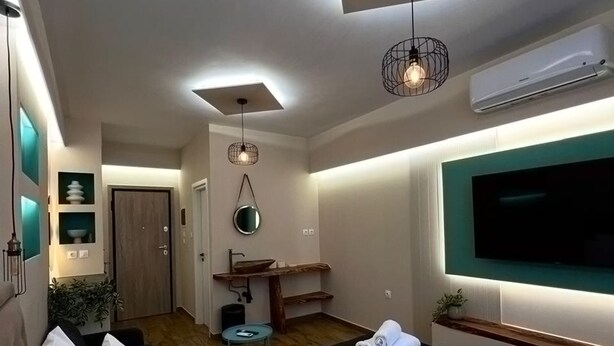 Ein modernes Hotelzimmer mit einem großen Bett, einem an der Wand befestigten Fernseher, einem kleinen Badezimmer mit Waschbecken und Spiegel sowie einer Deckenleuchte.