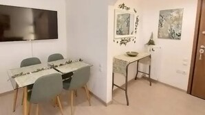 Un comedor con una mesa y sillas, un televisor de pantalla plana montado en la pared y una mesita con un cuenco y una lámpara.