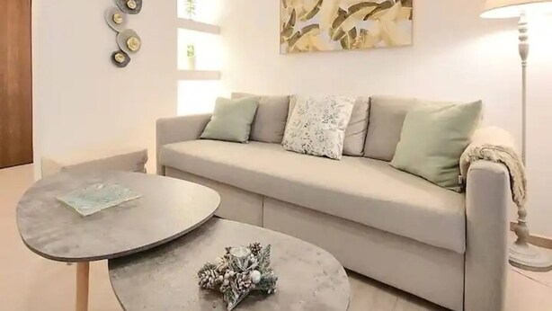 Una sala de estar moderna con un sofá gris, dos mesas redondas y un elemento decorativo en la pared.