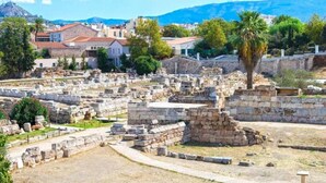 Un sitio arqueológico con ruinas y una vista despejada del paisaje circundante, incluyendo montañas y edificios modernos.