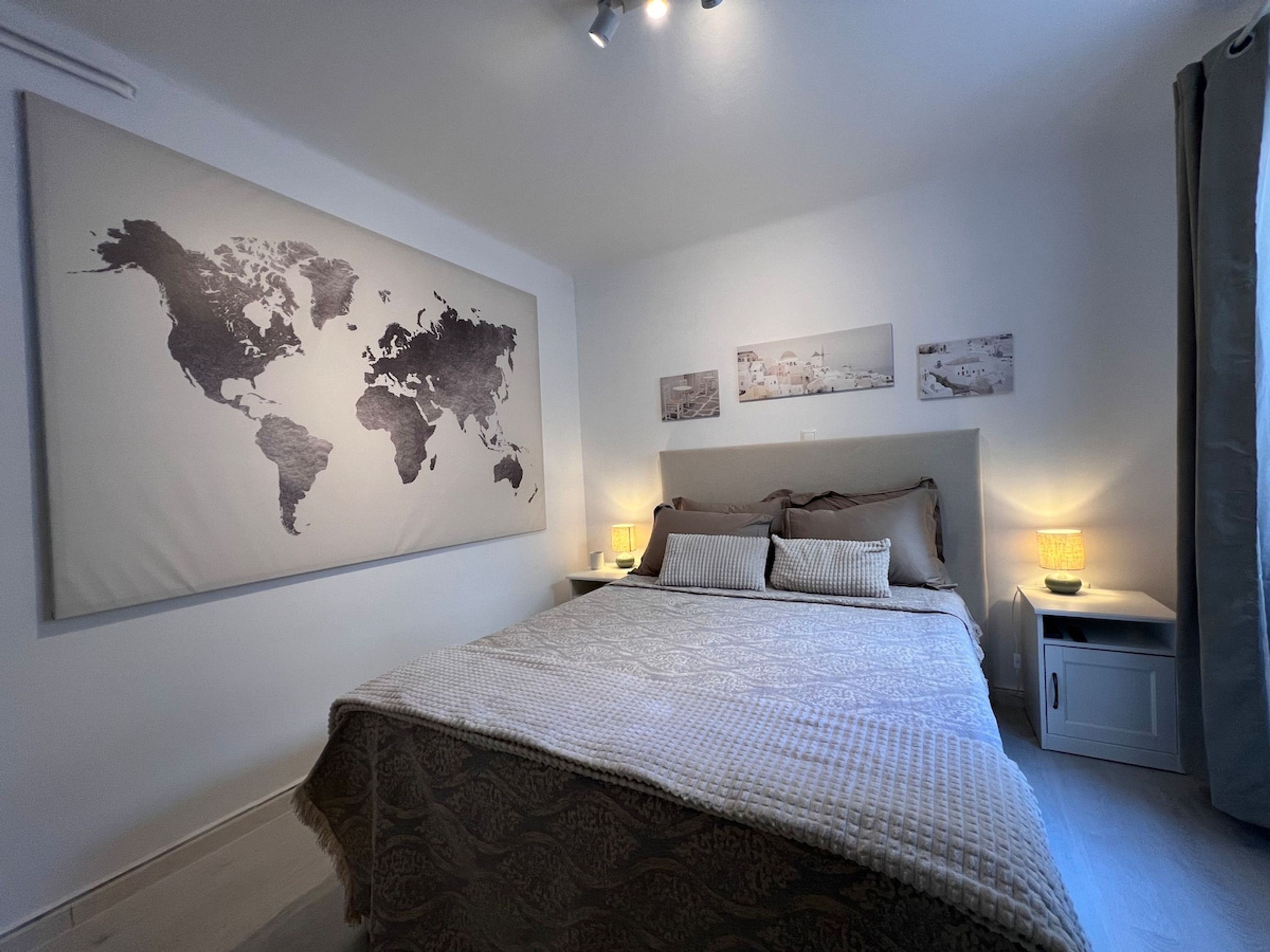 A bedroom with a large world map on the wall, a bed with patterned bedding, two bedside tables with lamps, and a nightstand with a lamp.