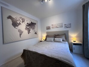 Ein Schlafzimmer mit einer großen Weltkarte an der Wand, einem Bett mit gemusterten Bettwäsche, zwei Nachttischen mit Lampen und einem Beistelltisch mit einer Lampe.
