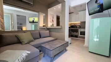 A modern living room with a grey sofa, a small ottoman, and a television mounted on the wall.